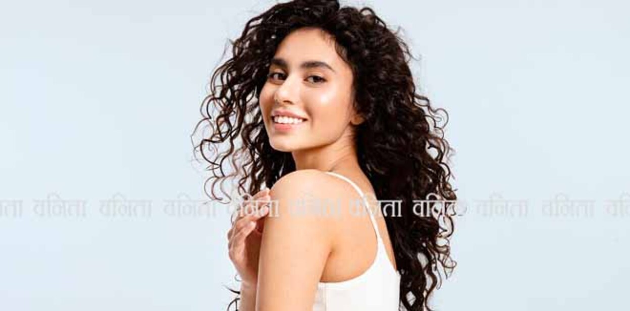 A model girl with glowing skin and thick black and curly hair looks over her shoulder at the camera against a blue background