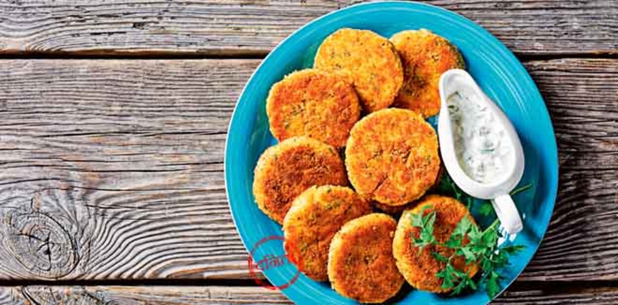 Easy fish cakes of white fish fillet: cod or haddock with potato and parsley, breaded in breadcrumbs served on a plate with tartar sauce in a gravy boat on a wooden background,  top view, close-up