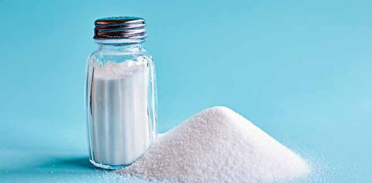 Spilled salt and saltshaker on blue background