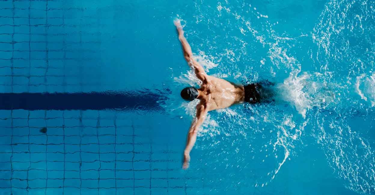 Aerial Top View Male Swimmer Swimming in Swimming Pool. Professional Determined Athlete Training for the Championship, using Butterfly Technique. Top View Shot