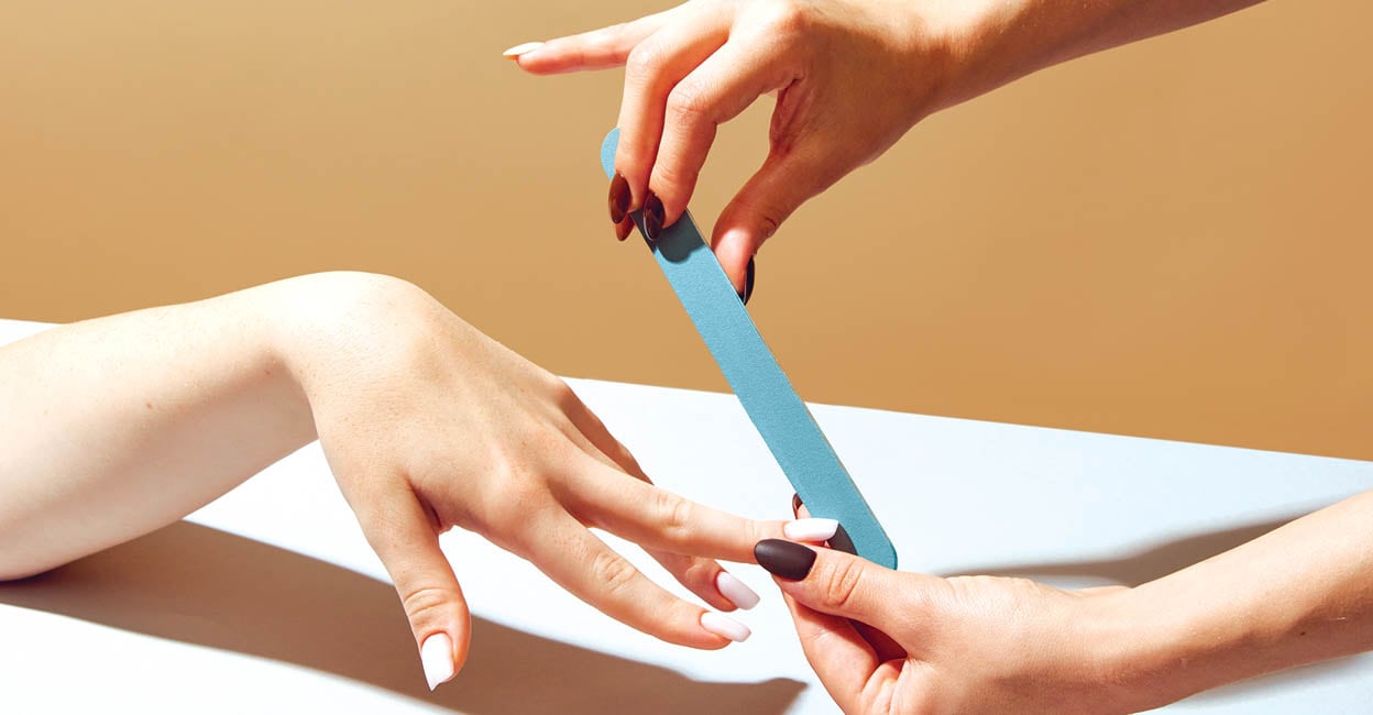 Female hand using nail file, taking care after hands, nails against beige background. Professional salon manicure. Concept of hand care, cosmetics and cosmetology, spa, natural beauty. Poster, ad