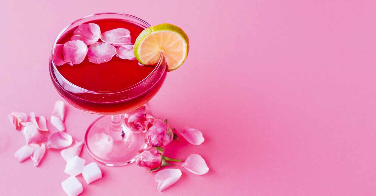 Cocktail bar background. Rose beverage with vodka, pineapple juice and strawberry champagne served with lemon slice and rose petals at pink backdrop, copy space