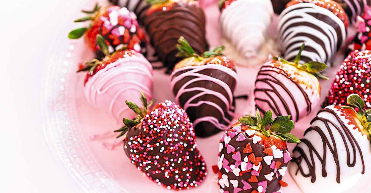 Variety of chocolate dipped strawberries on a pink cake stand.
