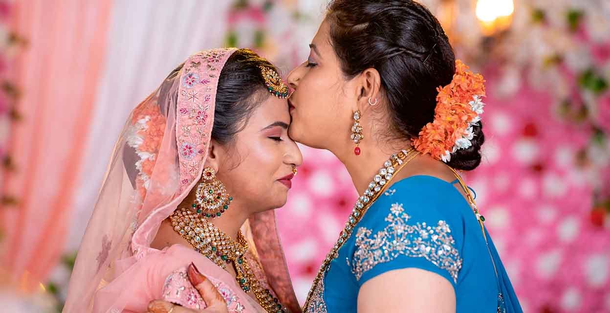 happy loving mother kissing daughters forehead by hugging her bridal daughter during wedding on stage - concept of Emotional Moment, parental blessings and traditional culture
