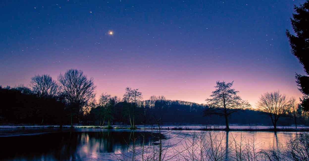 Dusk at winter evening with stars and venus on the night sky at lake landscape with silhouettes trees and reflection